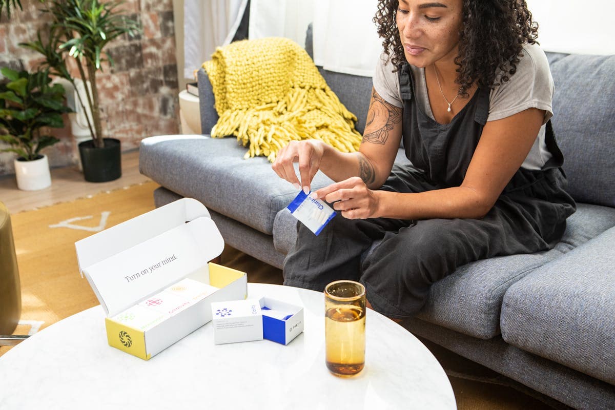 Woman at home checking a medication package — compare prices in 100+ pharmacies